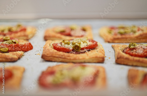 Baked square mini pizzas with salami, cheese, olives and tomato.