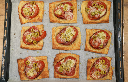 Baked square mini pizzas with salami, cheese, olives and tomato.
