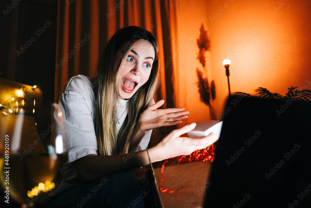 Young millennial woman open gift in front laptop computer during video call and drinking wine, use technology for communicate with friends or family. Young millennial woman open gift in front laptop computer during video call and drinking wine, use technology for communicate with friends or family.