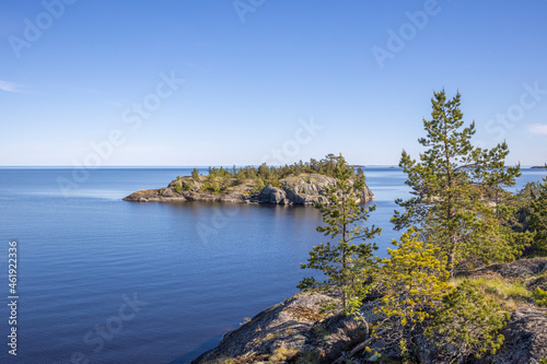 Sunny day at the lake. Reflection of the sky in the water. Pines on stones. The nature of the north. © Sergei