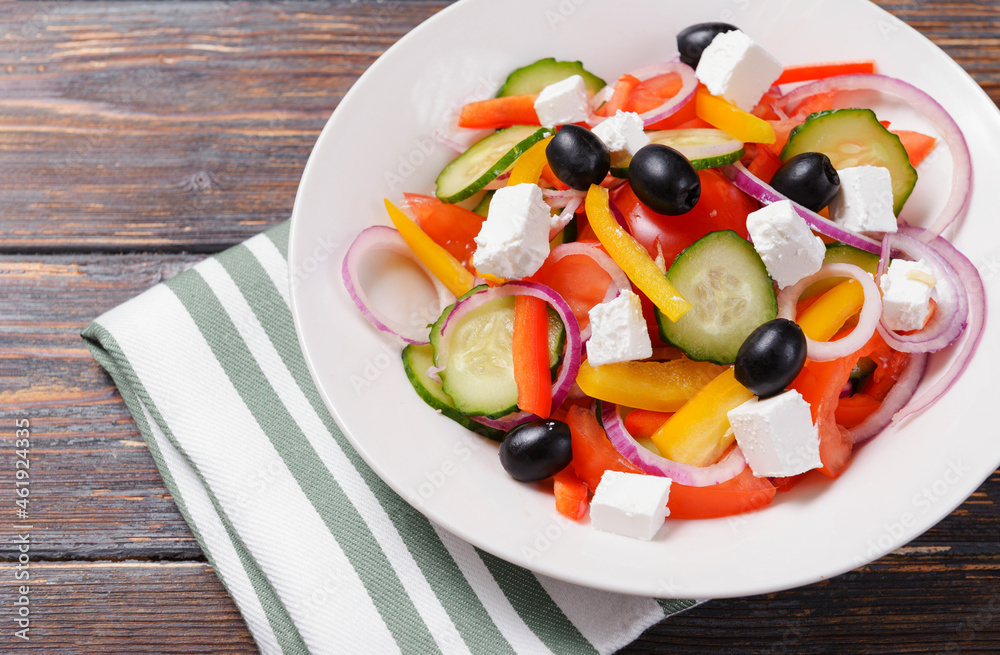 greek salad with tomatoes, cucumbers, olives, pepper and soft feta cheese in a  plate on a wooden