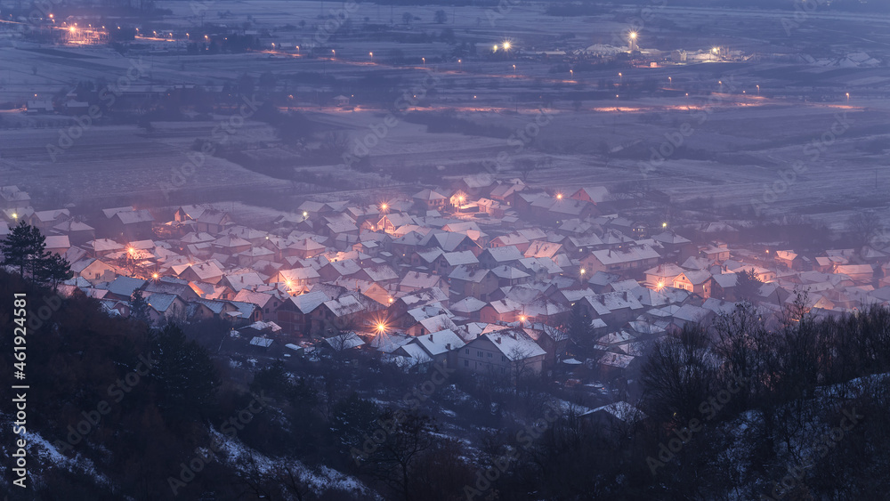 Obraz premium View from above of a dreamy, misty little village covered in snow during late blue hour
