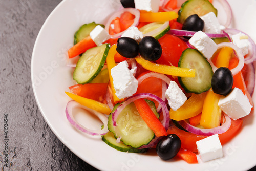 greek salad with tomatoes, cucumbers, olives, pepper and soft feta cheese in a plate on a dark