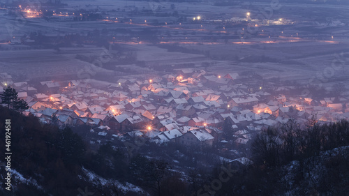 View from above of a dreamy, misty little village covered in snow during late blue hour