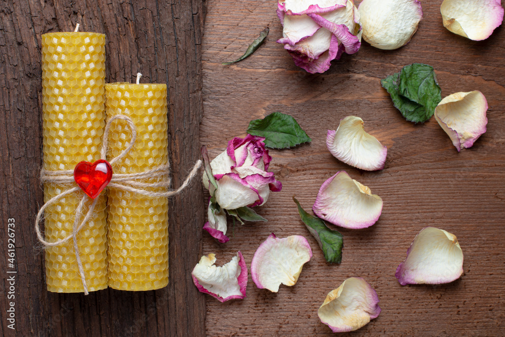 yellow wax candles on a wooden background with dried roses. handmade candles tied with a jute rope with a heart and rose petals.