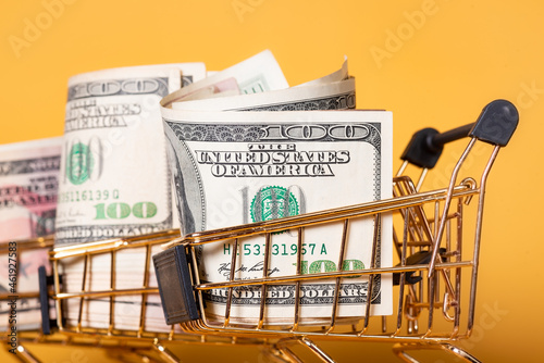 A cart of gold color with dollars in it on a yellow background. Finance concept.