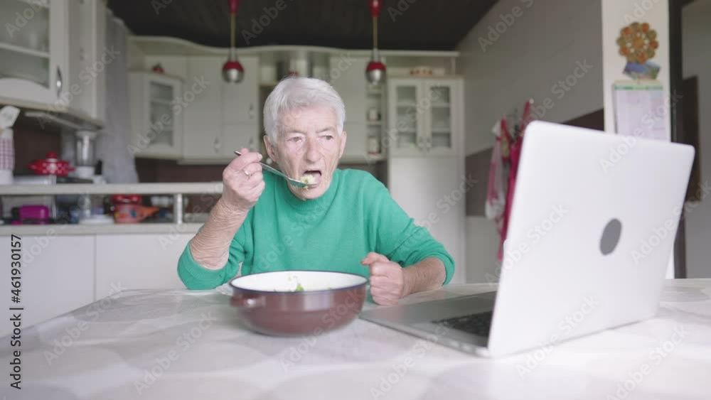 Slow motion - Old woman eating lunch at home and watching lap top Slow motion - Old woman eating lunch at home and watching lap top