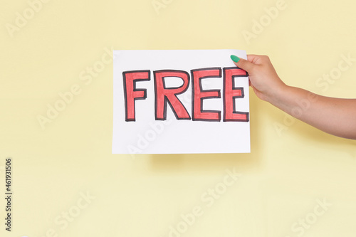 Latin woman's hand holding a sign with the word FREE on a white sheet, on yellow background, unrecognizable model.