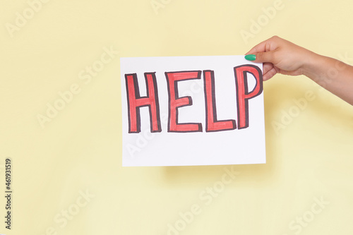 Latin woman's hand holding a sign with the word help written in red on a white sheet, on yellow background, unrecognizable model.
