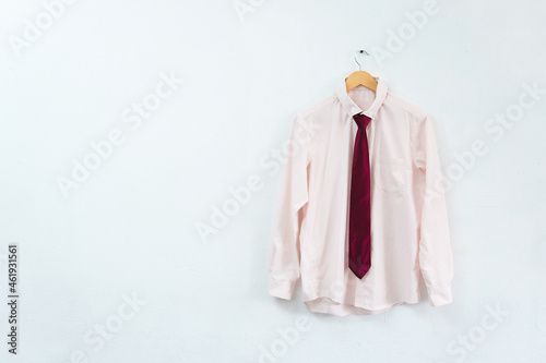 pink shirt with wine tie hanging on a wooden hook on a white wall, with copy space, not people.