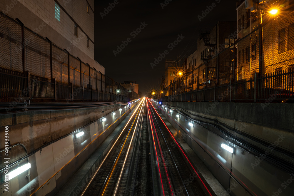Long exposure white and red light trails from the CTA trains departing and coming from an underground tunnel at night with alley lights and residential buildings on either side of the tracks.