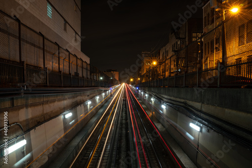 Long exposure white and red light trails from the CTA trains departing and coming from an underground tunnel at night with alley lights and residential buildings on either side of the tracks.