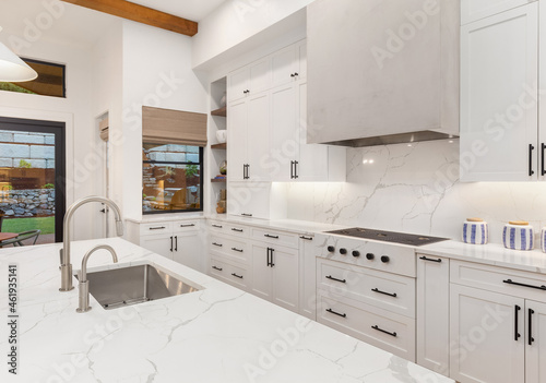 Beautiful white kitchen in new luxury home with large island. Features stainless steel appliances and sleek modern range hood.