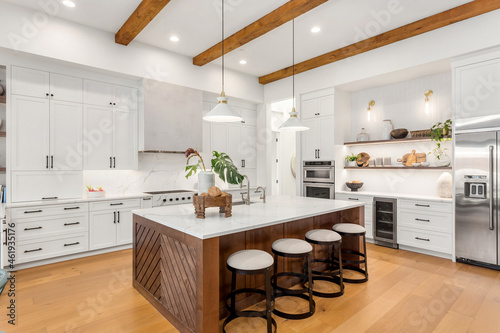 Beautiful white kitchen in new luxury home with large island. Features large island, stainless steel appliances, and sleek modern range hood.