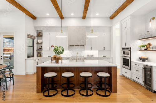 Beautiful white kitchen in new luxury home with large island. Features large island, stainless steel appliances, and sleek modern range hood.