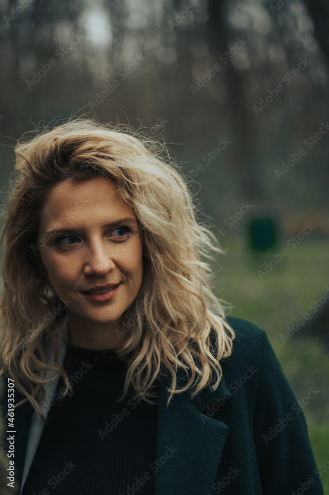 Young blonde woman walking in the woods in a green coat
