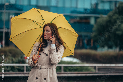Woman using smartphone and holding a yellow umbrella during a heavy rain in the city