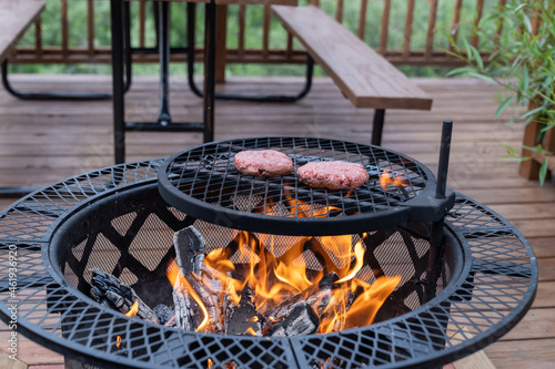 Ground beef hamburger patties cooking over an open flame on a grill at a campground patio