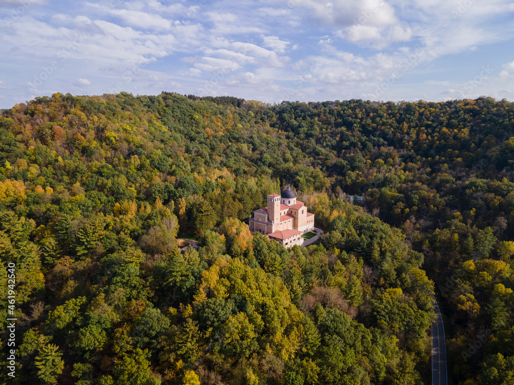 aerial view of shrine in forest on bluff during autumn in midwest on a sunny day; church nestled in the trees on mountain; beautiful blue sky 