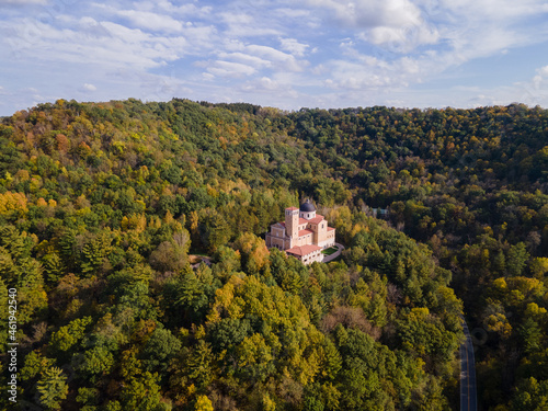 aerial view of shrine in forest on bluff during autumn in midwest on a sunny day; church nestled in the trees on mountain; beautiful blue sky 