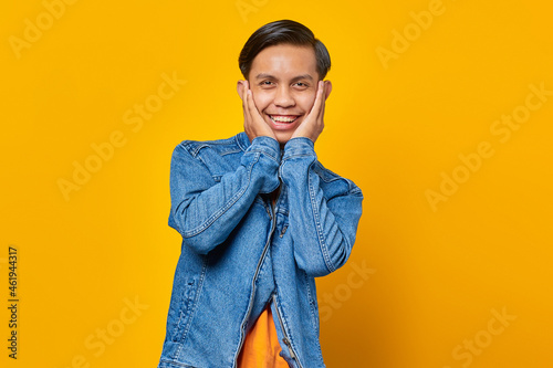 Portrait of surprised young Asian man looking at camera isolated on yellow background