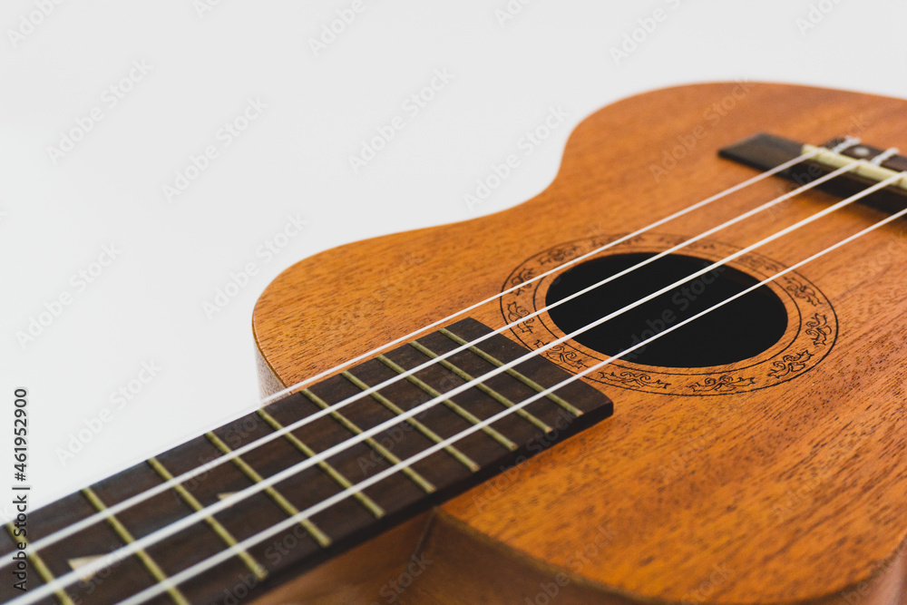Close up of brown Ukulele on white background. Ukulele strings, saddle, soundhole, ukulele body, neck, fretboard.
