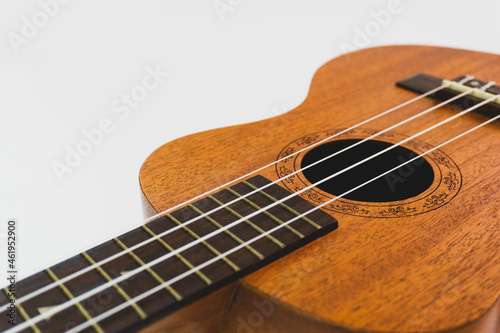 Close up of brown Ukulele on white background. Ukulele strings, saddle, soundhole, ukulele body, neck, fretboard.