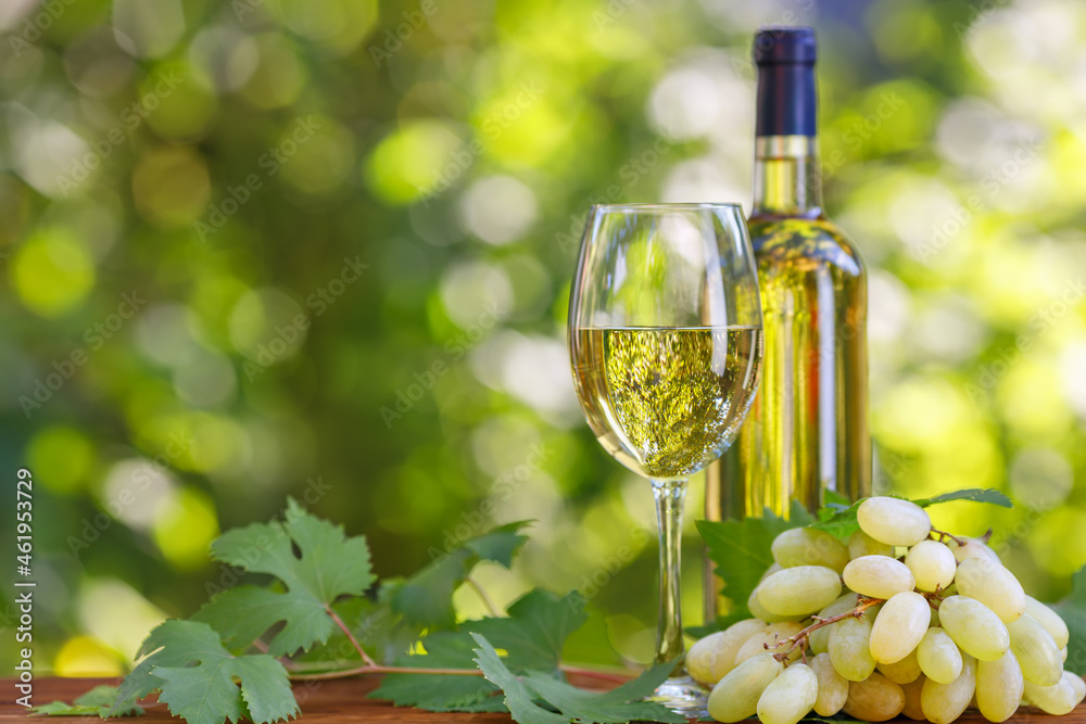 bottle and glass of white wine on wooden table in garden