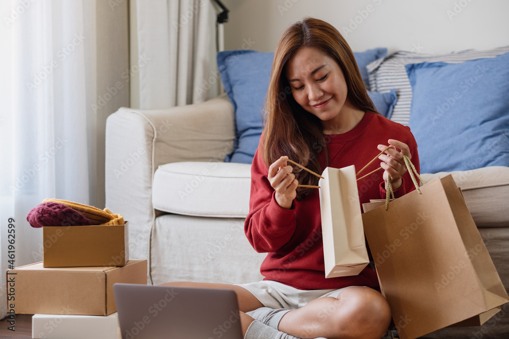 A woman using laptop for online shopping , holding shopping bags and opening postal parcel box at home A woman using laptop for online shopping , holding shopping bags and opening postal parcel box at home