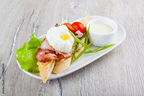 poached egg with bacon cherry tomatoes onion on a baguette and white sauce