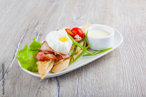 poached egg with bacon cherry tomatoes onion on a baguette and white sauce