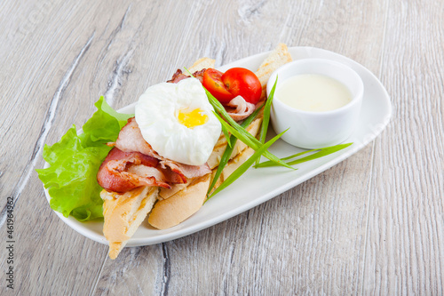 poached egg with bacon cherry tomatoes onion on a baguette and white sauce