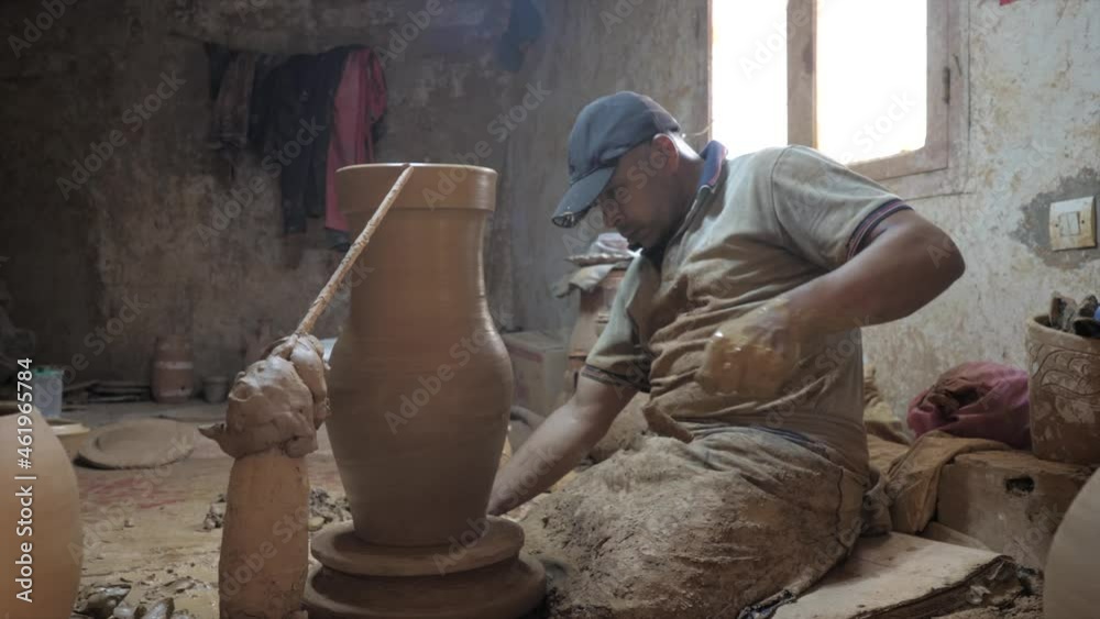 Potter giving final touches to the large clay vase on potters wheel. Side view. Potter giving final touches to the large clay vase on potters wheel. Side view.