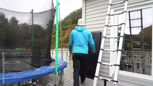 Person climbing down ladder and carrying solar panles outside private home during installation process - Static - Norway photo
