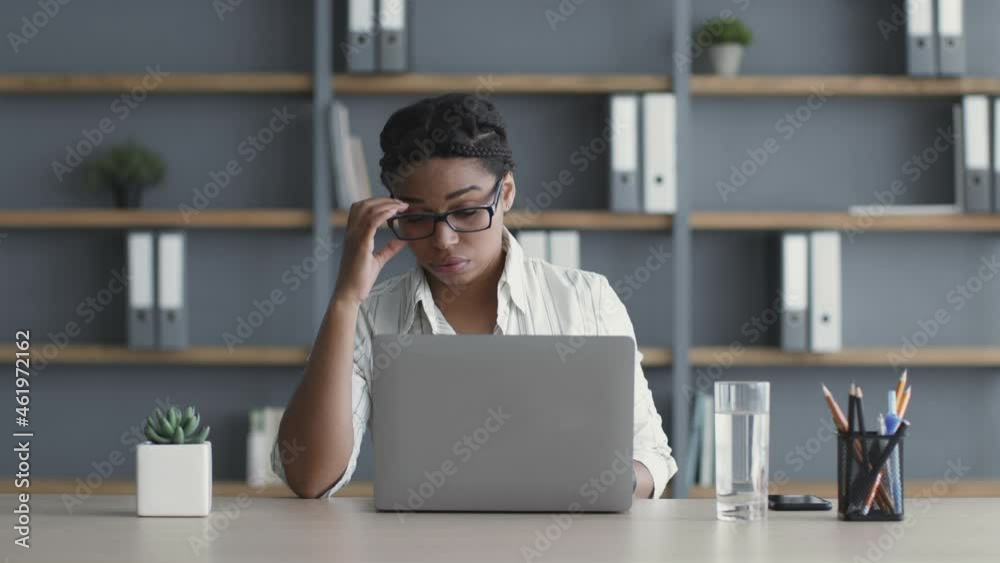 Young exhausted african american woman feeling tired at workplace, working on laptop extra hours at office