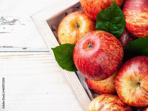 Close up of fresh organic apples and green leaves in wooden box on the white wooden background. Vertical. New Zealand gala variety. Copy space