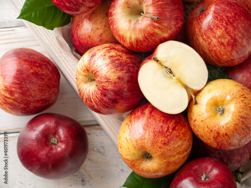 Close up of red and yellow organic apples in wooden box with green leaves on the white wooden background with sliced apple in the top. Top view. Horizontal. New Zealand gala variety.