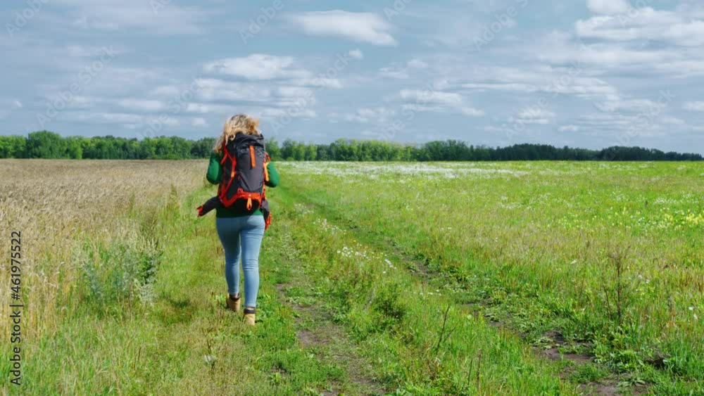 A young woman is walking along a country road with a cereal field. A backpacker or a hitchhiker is traveling on a nasty day A young woman is walking along a country road with a cereal field. A backpacker or a hitchhiker is traveling on a nasty day