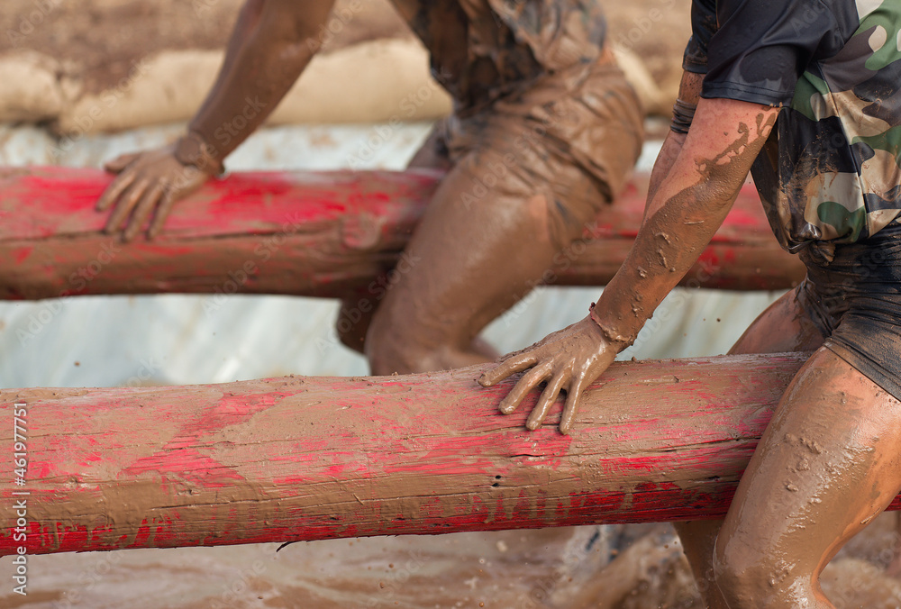 Mud race runners. Participants on the tree trunk, catches balance above the pit full of water
