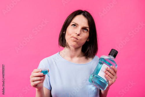 Beautiful girl uses mouthwash on the pink background photo