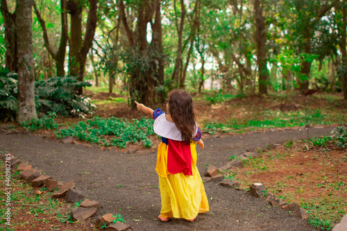 Cute little Hispanic girl wearing a Snow White dress as her Halloween costume in a forest