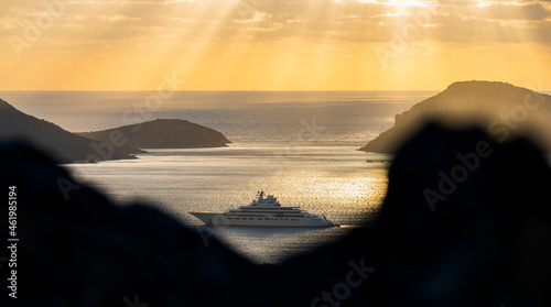Obraz na płótnie (Selective focus) Stunning sunrise during a cloudy day with a rock in the foreground and a luxury yacht sailing on a calm water in the distance. Golfo Aranci, Sardinia, Italy. w salonie