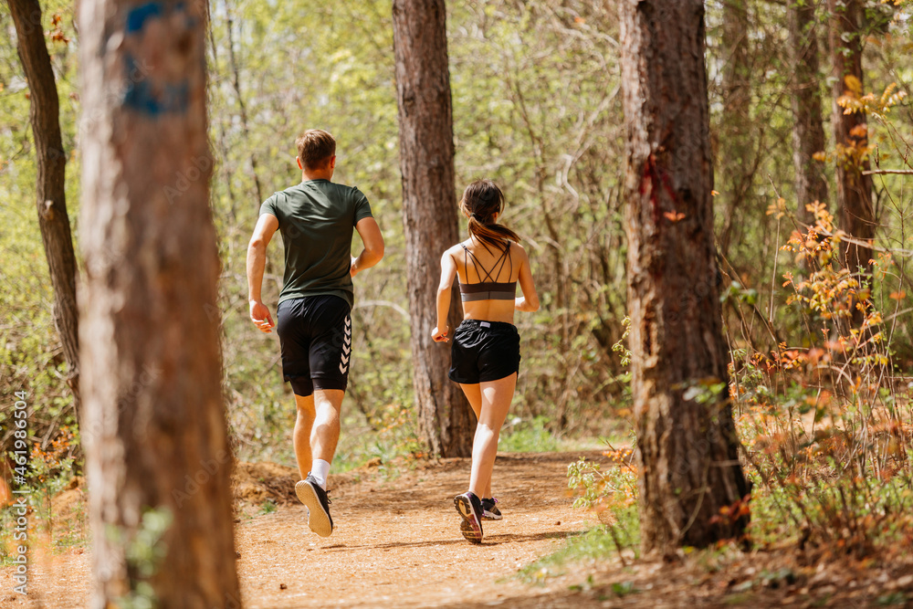 Man and woman exercising and jogging together at the park. Happy and smiling as they run along the path during sunset on a warm summer day Man and woman exercising and jogging together at the park. Happy and smiling as they run along the path during sunset on a warm summer day
