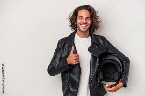 Young biker caucasian man holding a motorbike helmet isolated on gray background smiling and raising thumb up