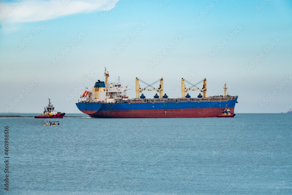 Fototapeta premium A cargo ship leaving the port with a guide
