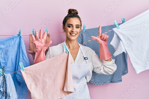 Beautiful brunette young woman washing clothes at clothesline showing and pointing up with fingers number seven while smiling confident and happy.