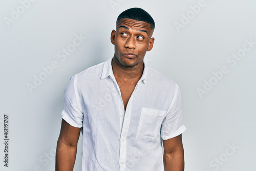 Young black man wearing casual white shirt smiling looking to the side and staring away thinking.