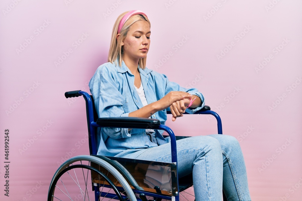 Beautiful blonde woman sitting on wheelchair checking the time on wrist watch, relaxed and confident Beautiful blonde woman sitting on wheelchair checking the time on wrist watch, relaxed and confident