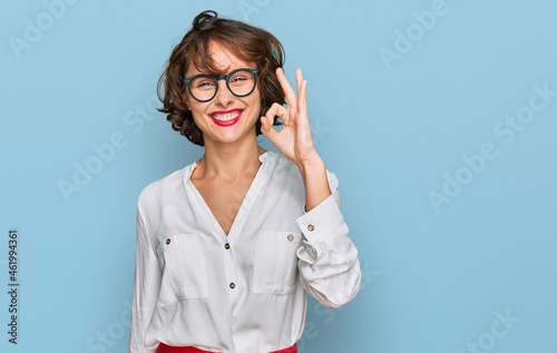 Young hispanic woman wearing business style and glasses smiling positive doing ok sign with hand and fingers. successful expression.