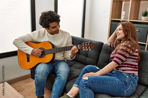 Young couple smiling happy playing classical guitar sitting on the sofa at home.